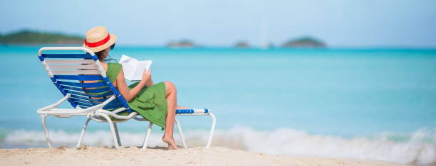 istock Young woman reading book on chaise-lounge on the beach 926829204