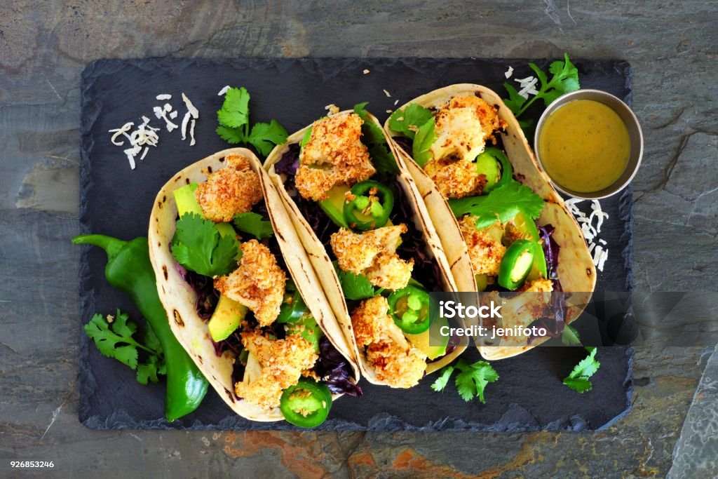 Healthy coconut cauliflower tacos, above on dark slate Roasted coconut cauliflower tacos. Healthy, vegan meal. Above view on a dark slate stone background. Taco Stock Photo