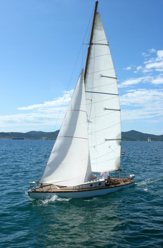 Bodrum,Mugla, Turkey. March 23,2019 sailor team driving sail boat in motion, sailboat wheeling with water splashes, mountains and seascape on background. Sailboats sail in windy weather in the blue waters of the Aegean Sea, on the shores of the famous holiday destination Bodrum