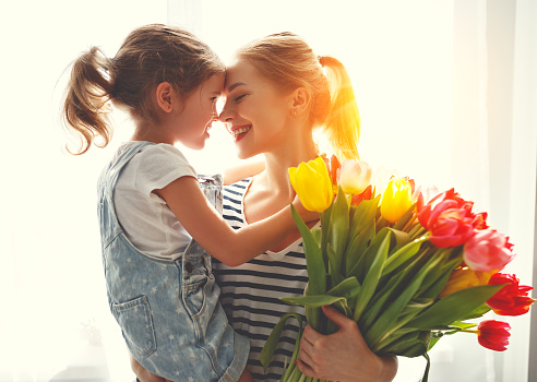 happy mother's day! child daughter congratulates mother and gives a bouquet of flowers to tulips
