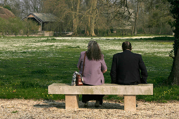 Essen, Germany - May 25, 2014: Capture of senior people at river Ruhr in spring. Scene is on promenade of river in Essen Kettwig. Three women are sitting on bench. They are talking. In background a couple is standing close to river.