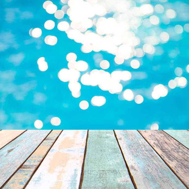 istock Perspective wood table top and Soft focus bokeh light effects over a rippled, blue water background in the pool, product display montage 926901860