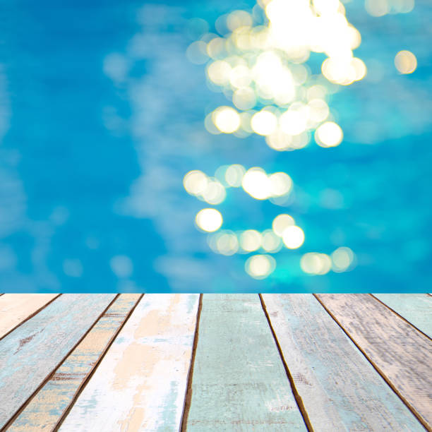 istock Perspective wood table top and Soft focus bokeh light effects over a rippled, blue water background in the pool, product display montage 926901864