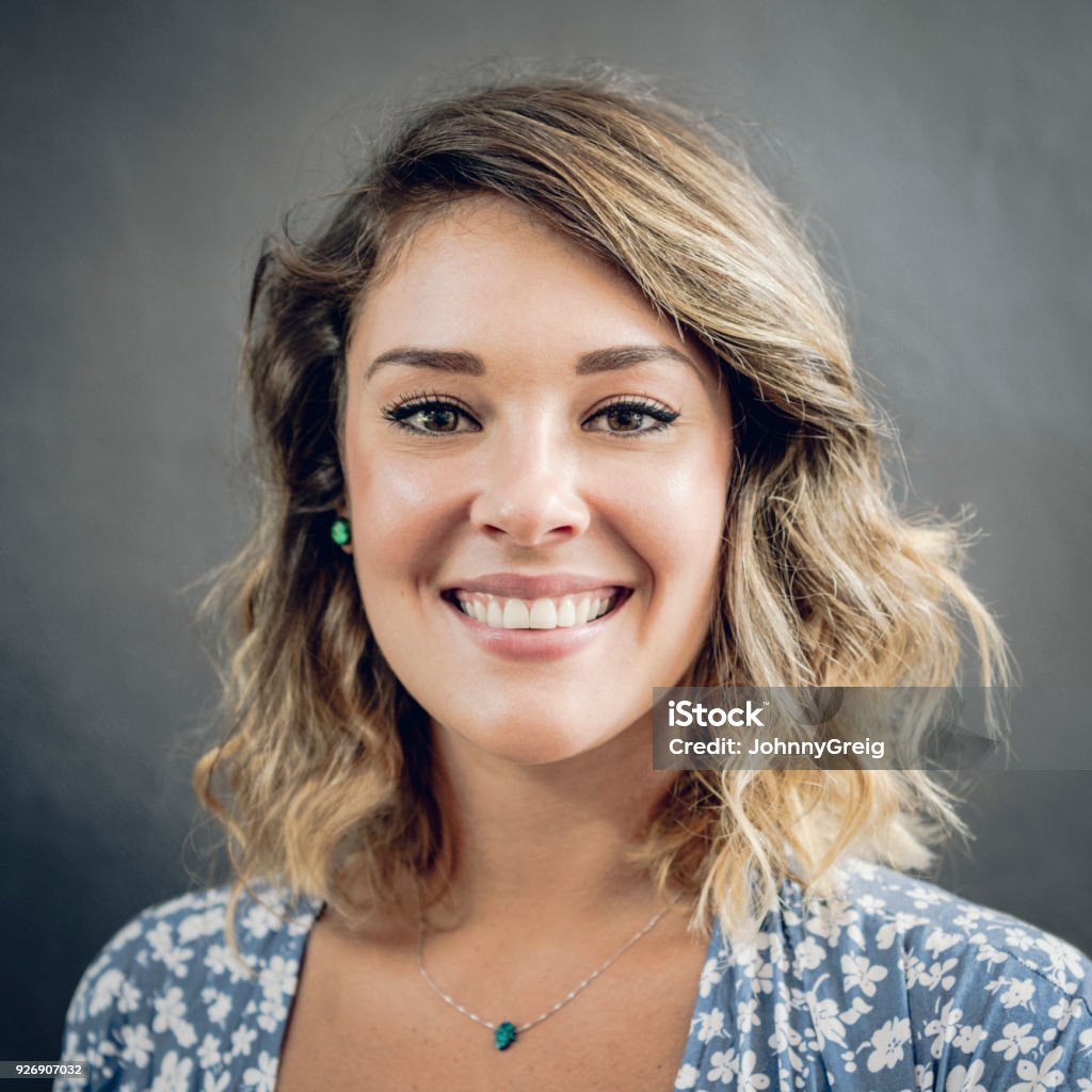 Portrait of attractive young woman smiling Head and shoulders view of woman in her 20s looking to camera with blonde wavy hair and necklace Women Stock Photo