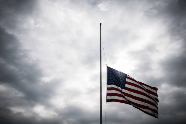 American Flag lowered to Half-Mast honoring a memorial American Flag lowered to Half-Mast honoring a memorial with a dramatic cloudy sunlight background moment of silence stock pictures, royalty-free photos & images