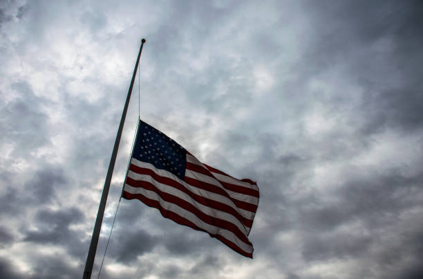 istock looking up at American Flag lowered to Half-Mast remembering those who served with a dramatic cloud background 926921728