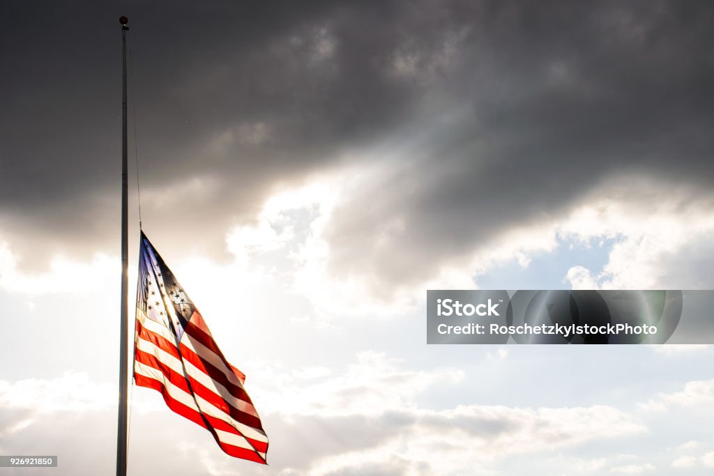 Perfect American Flag lowered to Half-Mast waving in the wind fully extended after another sad memorial Perfect American Flag lowered to Half-Mast waving in the wind fully extended after another sad memorial the flag glowing illuminated by bright sunshine Half-mast Stock Photo