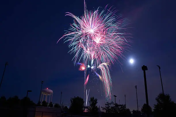 Fireworks display in summer with full moon and water tower in background.