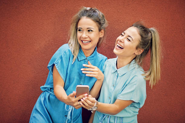 istock Happy twin sisters are laughing and browsing using mobile phone together 926930076