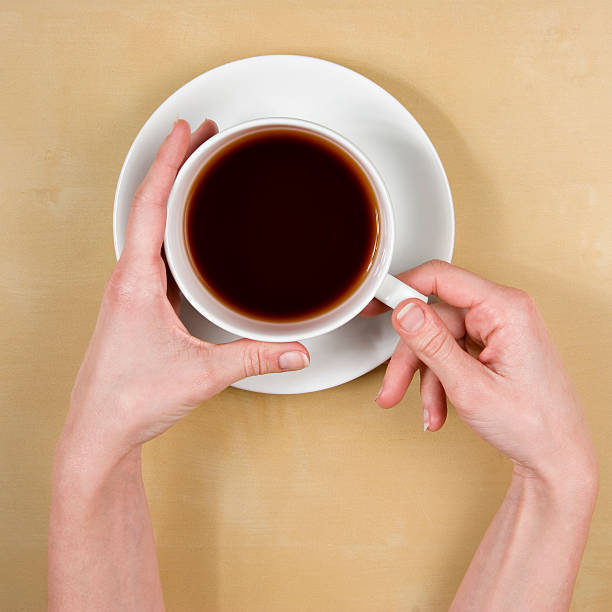 female hands holding a cup of coffee on wood table stock photo
