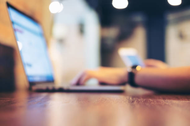 Blur image of a business woman holding mobile phone while using laptop in office