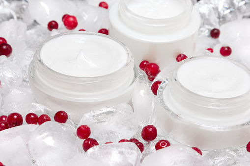 Natural skin care products with cooling effect. Glass jars of cream surrounded by ice cubes and red berries