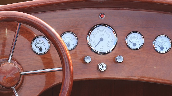 A vintage wooden speedboat's dashboard displaying all the controls and the steering wheel
