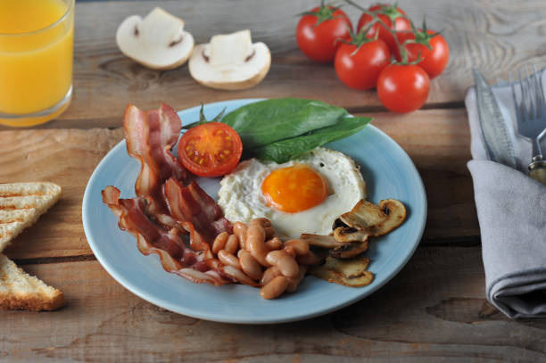 Breakfast of eggs with bacon, beans, mushrooms, tomatoes and spinach - on a wooden Board