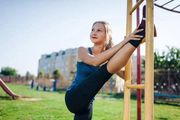 Photo of A woman in sportswear doing warming-up exercises. City in sunny evening.Fit fitness woman doing stretching exercises outdoors. Young blonde woman stretching.