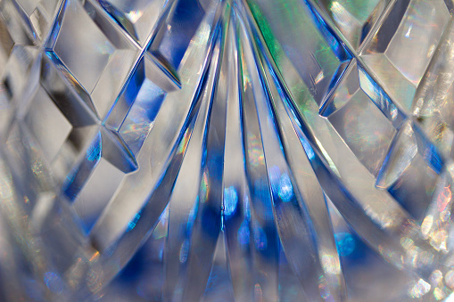 This abstract image features a close up view of lead crystal glass with fan and diamond shape facets reflecting vibrant blue color in natural light.