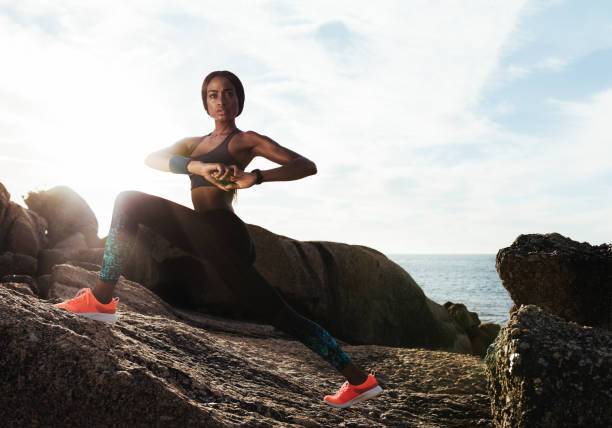 Fit young female runner doing stretches. Young woman stretching outdoors on rocks at beach.