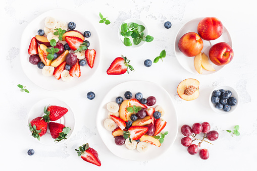 Fruit salad with strawberry, blueberry, peach, banana, grape and fresh fruits on white background. Flat lay, top view