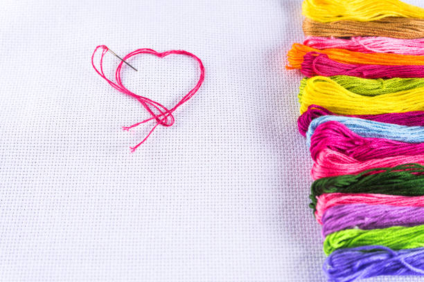 istock Colored thread for embroidery on white canvas, a needle with red thread in the shape of a heart. The concept of love for a hobby. Copy spase 926985690
