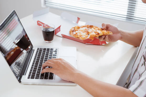 istock close up man hand eating pizza while working in laptop computer 926993098