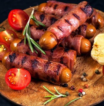 Festive cocktail sausages wrapped in crispy smoked bacon commonly known as 'Pigs in Blankets' on a black background