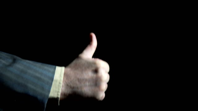 Hand of a businessman showing a gesture of a thumbs up on a black background