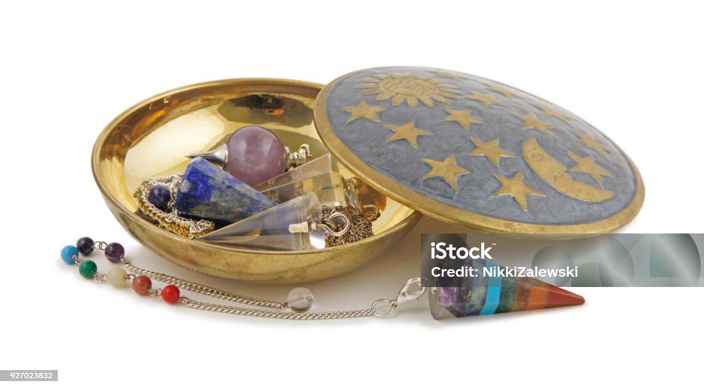 Selection of Radionics Dowsing Pendants Brass dish on a white background containing three different dowsing pendulums and one Chakra coloured pendant laid in front Spiral Stock Photo