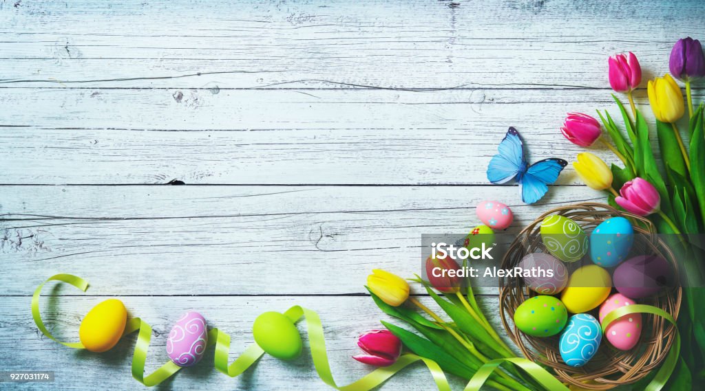 Easter background. Colorful spring tulips with butterflies and painted eggs Easter background. Colorful spring tulips with butterflies and painted eggs on vintage wooden board Easter Stock Photo
