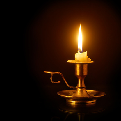 Stock photo showing close-up, nighttime view of a candle flame in a glass hurricane lamp on an al fresco restaurant table in the dark.