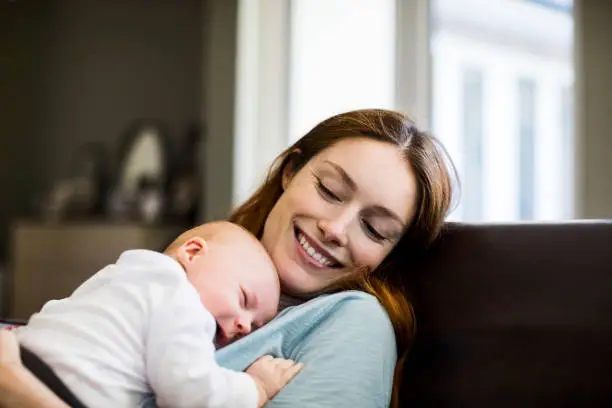 Photo of Smiling mother with sleeping newborn son on sofa