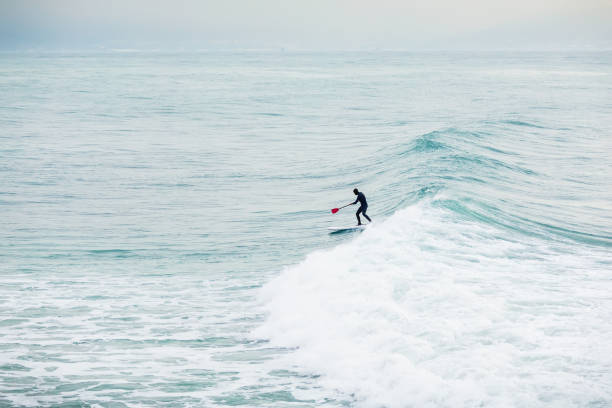 istock Surfer on stand up paddle board on blue wave. Winter surfing in ocean 927043272