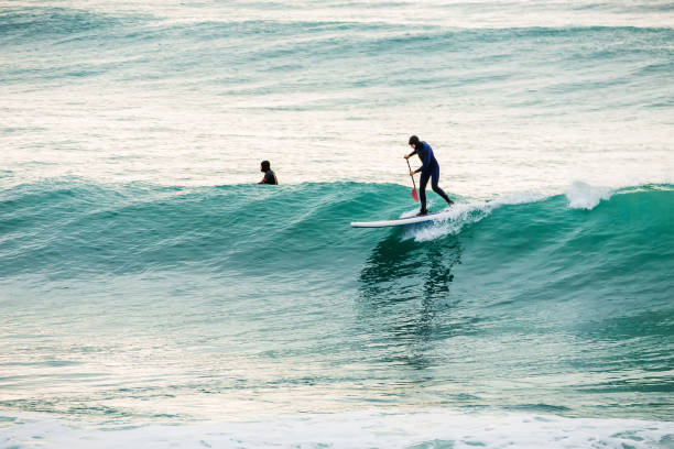 istock Surfer on stand up paddle board on blue wave. Winter surfing in sea 927043322