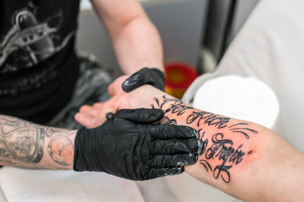 Man rubbing ointment to skin damaged by tattooing Tattoo artist rubbing ointment to skin damaged by tattooing. Unrecognizable Caucasian men. forearm tattoos men stock pictures, royalty-free photos & images