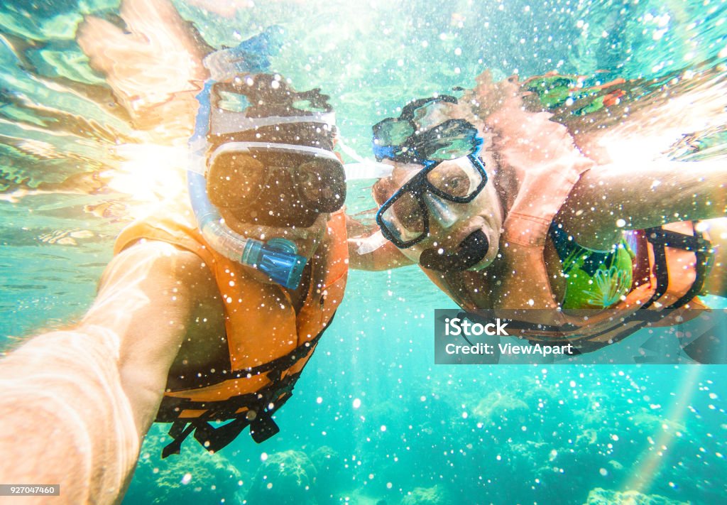 Senior happy couple taking selfie in tropical sea excursion with water camera - Boat trip snorkeling in exotic scenarios - Active retired elderly and fun concept on scuba diving - Warm vivid filter Fiji Stock Photo