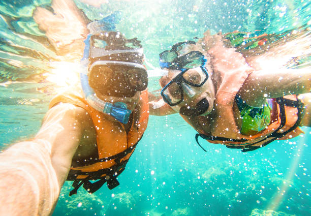資深快樂夫婦採取自拍在熱帶海遊覽與水觀景窗-小船旅途浮潛在異乎尋常的情況-活躍退休的老人和樂趣概念在水肺潛水-溫暖生動的篩檢程式 - 伯利茲 個照片及圖片檔