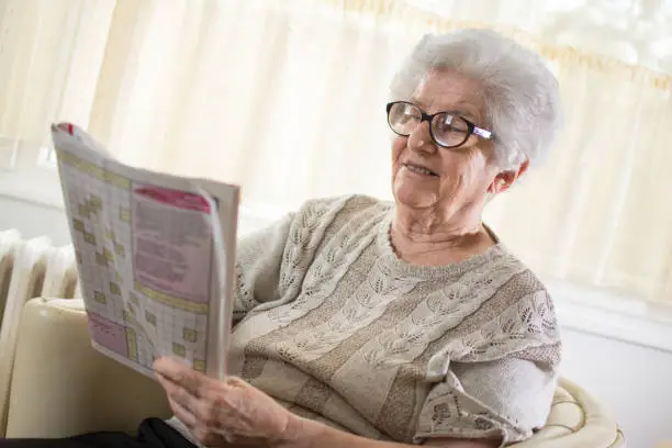 Happy senior woman solving a crossword puzzle at home.