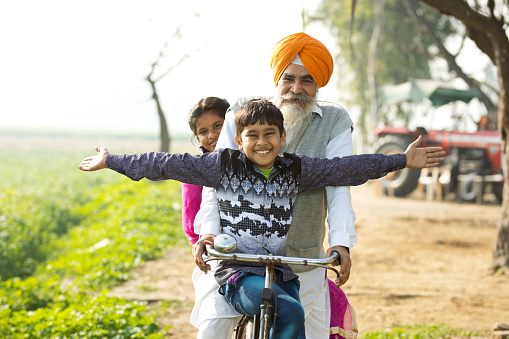 Portrait of Indian farmer with children riding bicycle on rural field