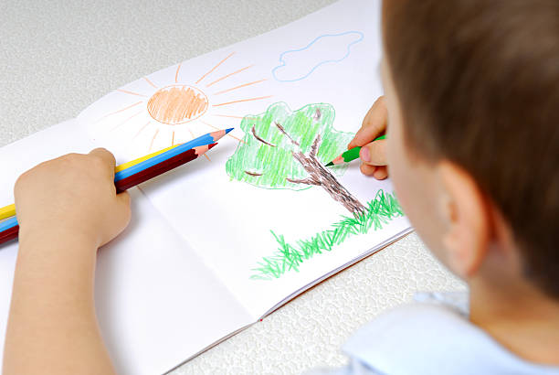 Boy drawing a tree grass and sun with colored pencils stock photo