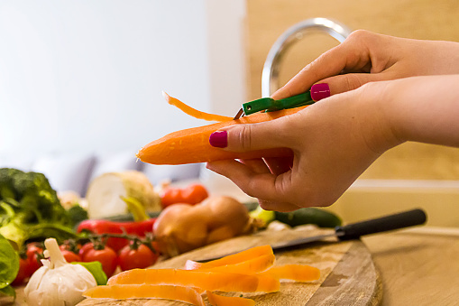 Female woman hands peeling carrots. Vegetarian healthy food. Preparation of fresh salad in a modern kitchen interior, healthy food concept. Selective focus.