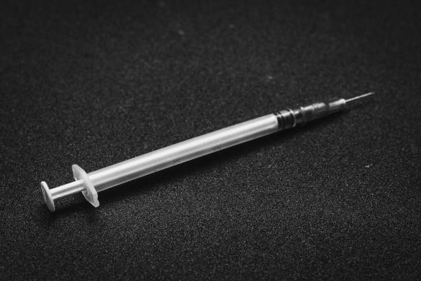 Plastic syringe on black asphalt, drug use. stock photo