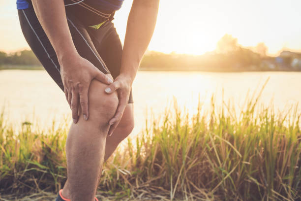 Injury from workout concept : The asian man use hands hold on his knee while running on road in the park. Shot in morning time, sunlight and warm effect with copy space for text or design lesiones por concepto de entrenamiento: hombre asiático uso manos sostienen sobre sus rodillas durante la ejecución de la carretera en el parque. disparo en efecto tiempo, luz solar y caliente de la mañana con espacio de copia de texto o diseño