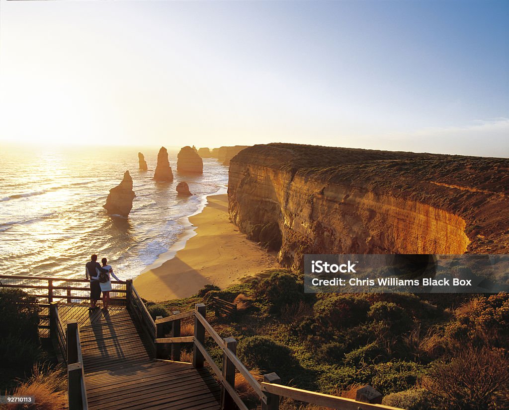 Romantic sunset over the sea. Man and woman admiring the sea at sunset.  In the distance are the Twelve Apostles, unique rock formations that rise out of the sea along the Victorian coast. Australia Stock Photo