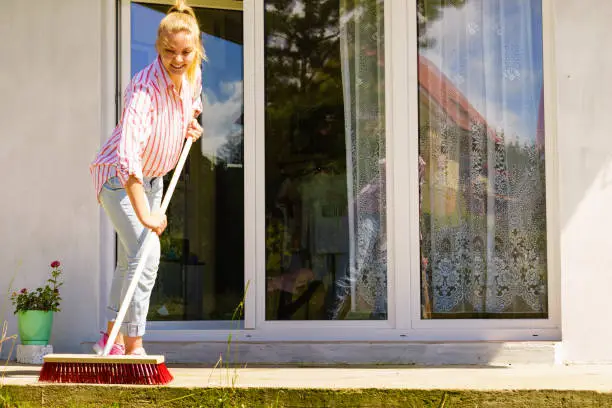 Female adult young woman using big broom to clean up backyard patio