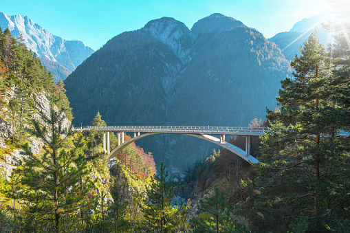 Bow shaped bridge over the river close to a road that is headed to Mangart saddle high in Julian alps on a sunny beautiful autumn day with colorful scenery and sun rays