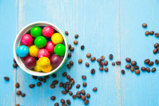 Love Coffee Concept. Blue wooden background with coffee beans and a bowl of round colorful candies, close up, top view