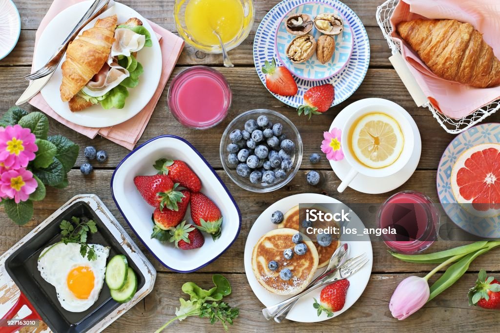 Breakfast food table. Festive brunch set, meal variety with fried egg, pancakes, croissants, smoothie ,fresh berries and fruits Breakfast food table. Festive brunch set, meal variety with fried egg, pancakes, croissants, smoothie ,fresh berries and fruits. Overhead view Springtime Stock Photo