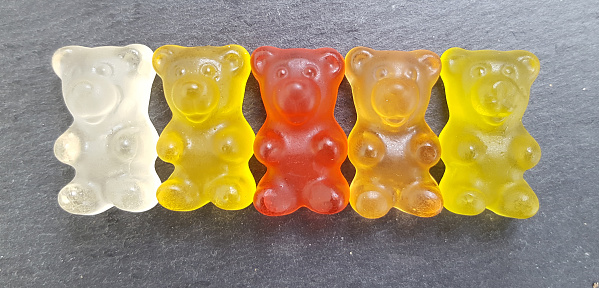 Various colored gummy bears in a row on dark stone background
