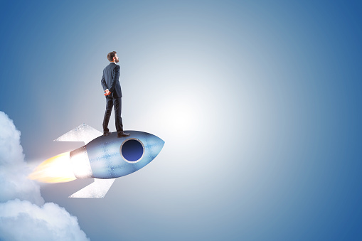 Businessman standing on launching rocket on abstract gray background with copy space. Start up and entrepreneurship concept