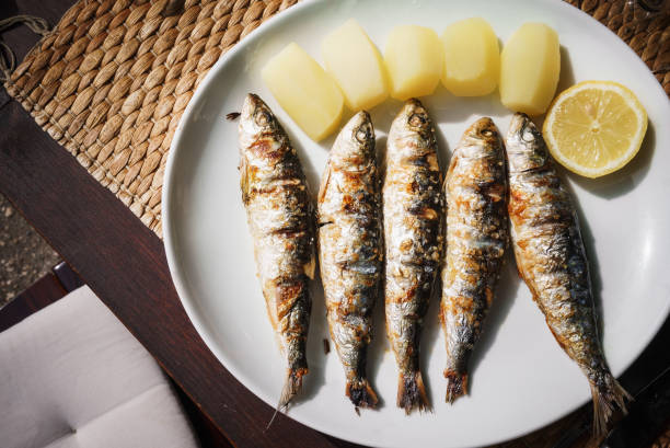 Fried appetizing mackerel, a slice of lemon and yellow potatoes lie on a white plate, standing on a wooden table. stock photo