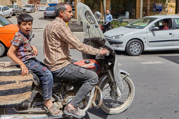 Kashan, Iran - April 27, 2017: Iranian man with his son is riding a motorcycle on a busy street.